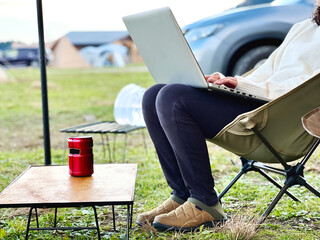 キャンプ場の車の横でノートパソコンを操作する女性