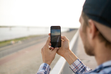 young male person tourist with smartphone taking a photo of city scene