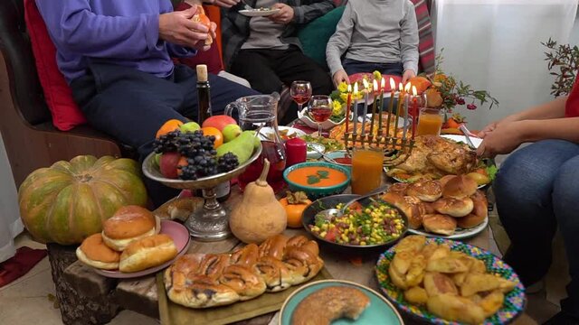 Authentic Jewish family celebrates Hanukkah night and have dinner together at home. Traditional kosher food and drinks on the festive table. Menorah with burning candles