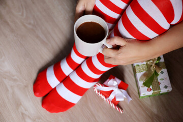 Girl in Christmas knee socks sitting with cup of hot cocoa in hands near the gift boxes. Cozy home atmosphere at winter, New Year celebration