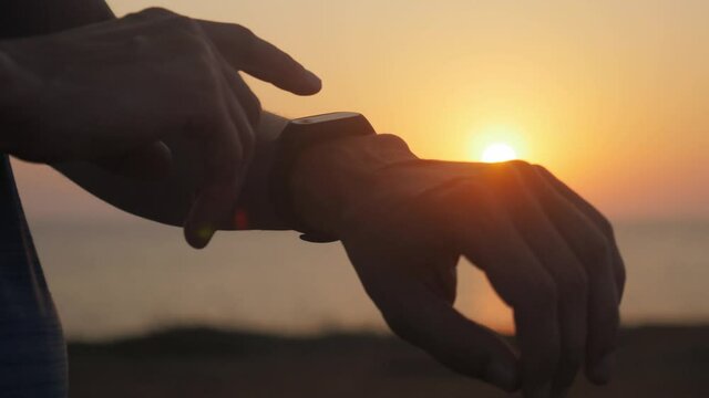 closeup of male hand arm with smart watch checking time results of outdoor sport training activity in summer sunset