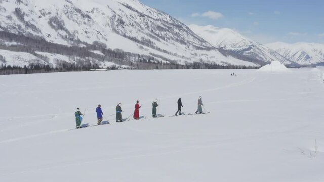 Aerial shot of a group of Tuva men dressed in deel walking in skis in snow covered steppe. Winter day in Hemu Village, Xinjiang, China.