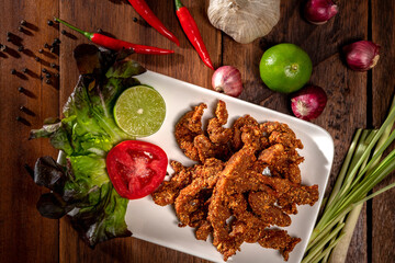 Top view, Fried pork on white plate with many herbs. Delicious recipe from Asia and spices ingredients on wooden table background. Thai spices food, Asian traditional foods, Thailand restaurant menu
