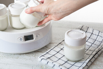 A woman's hand takes out a jar of ready-made Greek yogurt from a yogurt maker.