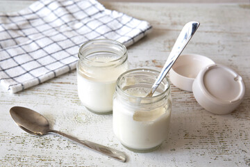 Two open jars of domestic yogurt sit on a shabby table at home. Healthy organic food concept.