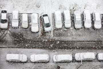 Cars in a row on a parking lot covered with snow, top view. Snowfall in a city