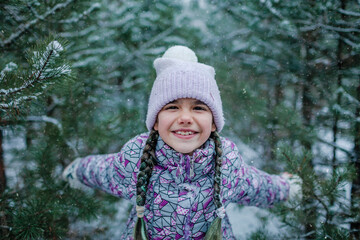 Pretty girl in warm clothes, with frozen mittens enjoys the first long-awaited snow during family...