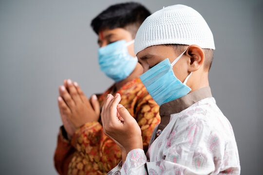 multiethnic kids with medical face mask praying together by folding hands to protect from coronavirus pandemic - Concept of friendship, communal harmony during covid-19 outbreak - Powered by Adobe