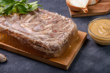 Chicken jelly on a board on a dark background, served with mustard and garlic.