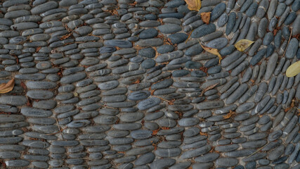 Sidewalk or footpath in the park made from gray stone covered with fallen leaves. Cobblestone road road in the street. Convex textured stones background.