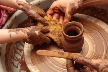 The child moulds from clay a pot on a potter's wheel. Adults help the child to work with clay.