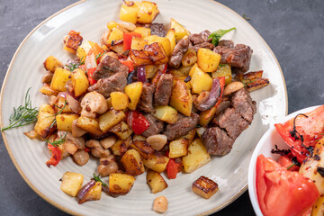 Fried potatoes with mushrooms and meat in a round plate close-up.