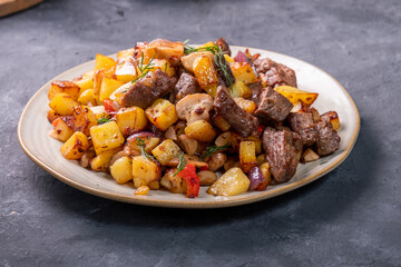 Roast with potatoes, mushrooms and pieces of meat in a plate, close-up.