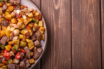 Large plate of fried potatoes with meat, mushrooms and onions and bell peppers. Top view, free space.