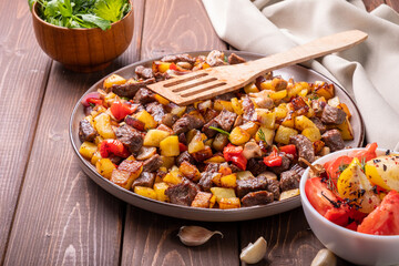 A large dish with roast potatoes, mushrooms and beef meat on a wooden background.