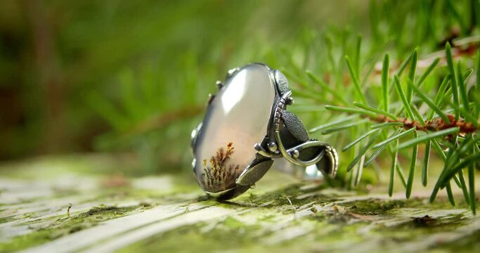Handmade silver ring with moss agate stone. The piece of jewelry rotates against the background of a spruce branch.