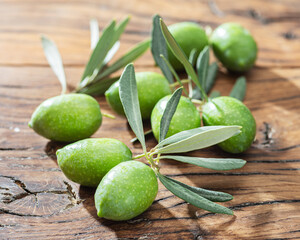Green natural olives with olive leaves on a vintage old wooden table.