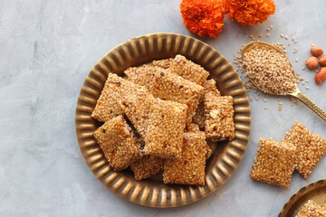 Indian makar sankranti or Lohri festival sweets. Tilgul in a small brass plate. Tilgul is made out of sesame seeds, peanuts, ghee, and jaggery. Til gud chikki or sesame candy. Copy Space. Winter food.