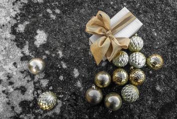 Festive packaging decorated with a bow. Nearby is a scattering of Christmas tree balls on an icy surface. Concept: celebration of Christmas and New year, Christmas decorations.