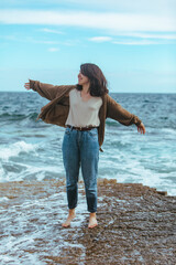 woman walking by rocky beach in wet jeans barefoot