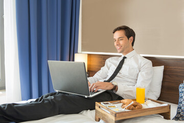 Fototapeta premium Happy businessman in suit working on the hotel bed on his computer laptop notebook