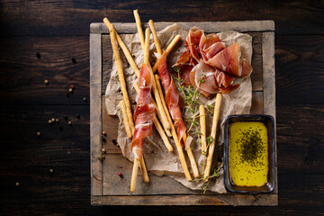 Traditional Spanish Jamon Serrano ham with grissini bread sticks, greens, olive oil. Prosciutto Crudo, Parma ham, Italian antipasto. Traditional snack on wooden table. Copy space. 
