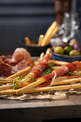 Traditional Spanish Jamon Serrano ham with grissini bread sticks, greens, olive oil. Prosciutto Crudo, Parma ham, Italian antipasto. Traditional snack on wooden table. Copy space. 