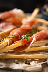 Traditional Spanish Jamon Serrano ham with grissini bread sticks, greens, olive oil. Prosciutto Crudo, Parma ham, Italian antipasto. Traditional snack on wooden table. Copy space. 
