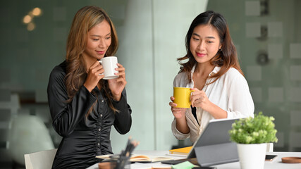 Businesswomen sip coffee while holding a small meeting in the office.