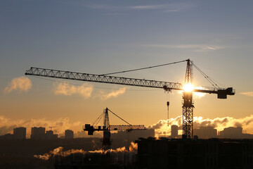Silhouettes of construction cranes and unfinished residential buildings on sunrise background. Housing construction, apartment block in city