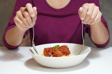 front view, woman holding spoon and fork and hot spaghetti in a white ceramic bowl, italian food