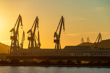 Fototapeta na wymiar Group of shipyard cranes against yellow sky at sunset in Ferrol, Galicia, Spain