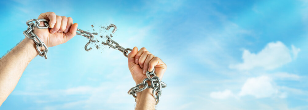 Male hands break the chains on blue sky background with copy space. Freedom concept.