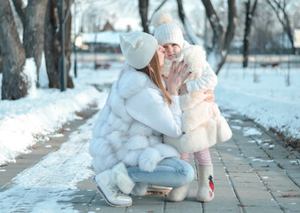 Happy family walks on snowy day. Little girl with her mother in winter park. A young and happy mother holds a child in her arms, smiles and rejoices. Street of winter fresh air, concept of recreation