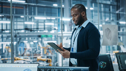 Car Factory Office: Portrait of Successful Black Male Chief Engineer Using Tablet Computer in Automated Robot Arm Assembly Line Manufacturing High-Tech Electric Vehicles. Side View Shot - obrazy, fototapety, plakaty