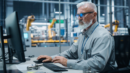 Fototapeta premium Car Factory Office: Portrait of Male Engineer Working on Computer. Automated Robot Arm Assembly Line Manufacturing Electric Vehicles. Technician Monitoring Electronics Production Conveyor.