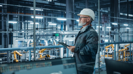 Car Factory Office: Portrait of Male Engineer Wearing Hard Hat Walking, Monitoring Production Conveyor with Tablet Computer. Automated Robot Arm Assembly Line Manufacturing High-Tech Electric Vehicles