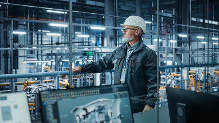 Car Factory: Confident Male Automotive Engineer Wearing Hard Hat, Standing and Monitoring Equipment Production Line. Automated Robot Arm Assembly Line Manufacturing Electric Vehicles