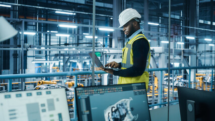 Car Factory: Professional Male Automotive Engineer Wearing Hard Hat, Walking, Using Laptop....