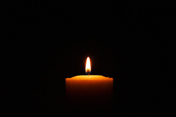 One single light candle burning brightly in the black background.Spiritual candle yellow flame. Flame of candle in the darkness.Copy space.