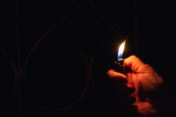 Woman hand holding a burning lighter in the dark black background.Closeup,selective focus.Copy...