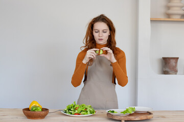 young girl in an apron makes a healthy salad of vegetables and herbs in her kitchen