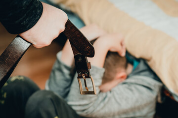 Family violence and aggression concept - furious man raised punishment fist with belt over scared child at home.Toned.