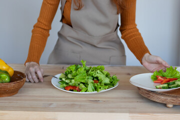 young girl in an apron makes a healthy salad of vegetables and herbs in her kitchen