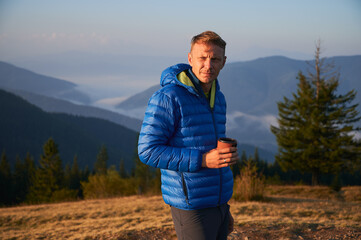 Male traveling on mountain meadows, squinting from bright sunlight, looking to the left against mountain beskids. Morning tourist walking on the fresh mountain air.