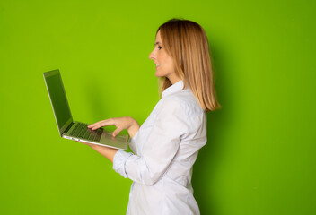 Portrait profile of young businesswoman holding silver laptop in the office isolated over green background
