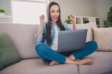 Portrait of attractive cheerful lucky long-haired woman sitting on divan using laptop rejoicing having fun at home indoors