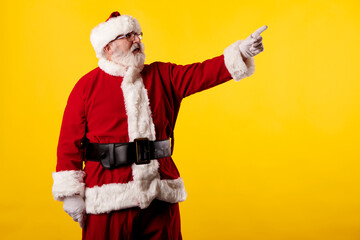 Fototapeta na wymiar Santa Claus pointing finger at billboard on yellow background