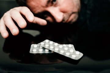 Narcotic addict white medicine pills on black table with reflection.The man tilted his head to look at the pills and take pills.