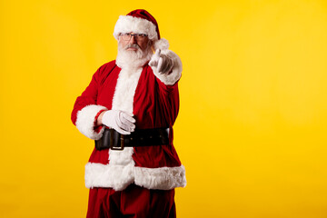 Fototapeta na wymiar Santa Claus pointing his finger at the camera on yellow background